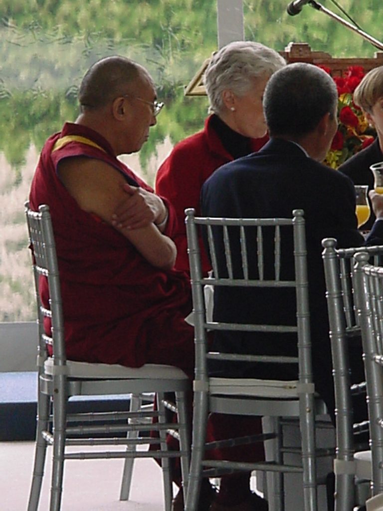 Event Description — Photo Gallery of The 14th Dalai Lama.
Custom Built Venue behind the home of the University of British Columbia President's residence, all built on a sloped hill.  This fine dining lunch was host to just over 100 Guests with white Glove service  These images are of the  but the Custom Built Foundation, a Custom Built, Clear sided tent, with light gray carpeting, Chiavari Silver Chairs, Pure White Linens, Orchids in the Dalai Lamas Colors of Maroon, Yellow and Purple, plus individual candle holders each with their own fruits facing outward for visual calmness of Oranges, Limes and Lemons.